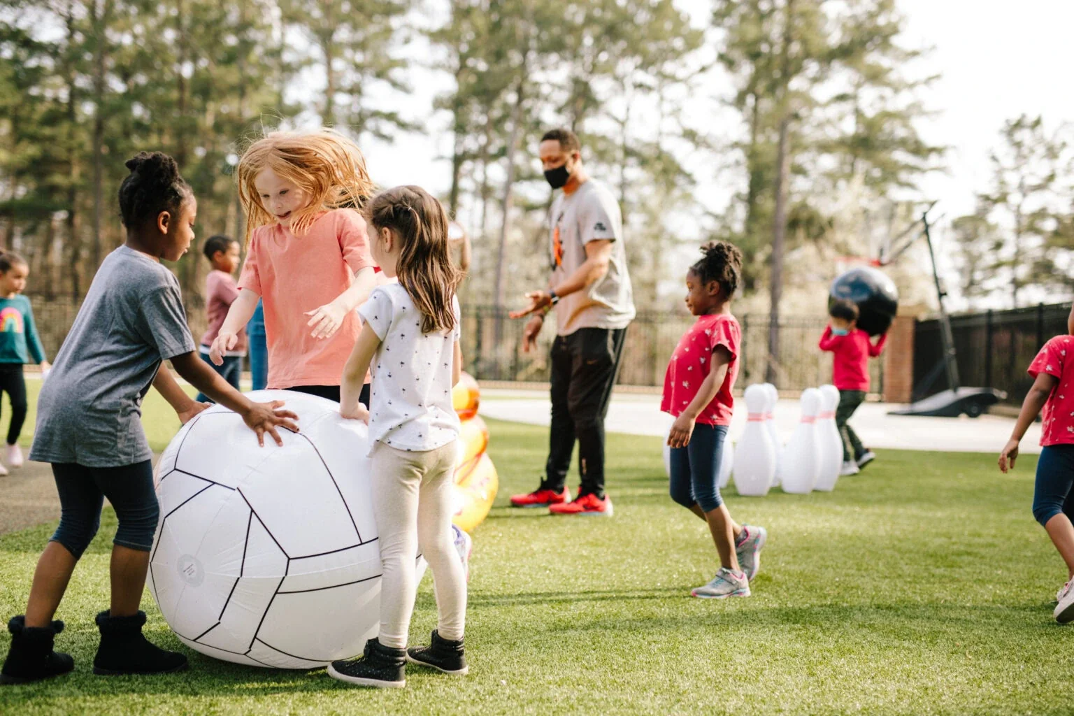 Children joyfully playing with a large soccer ball at a vibrant preschool in Alpharetta, Georgia, promoting teamwork, physical activity, and fun in a supportive learning environment.